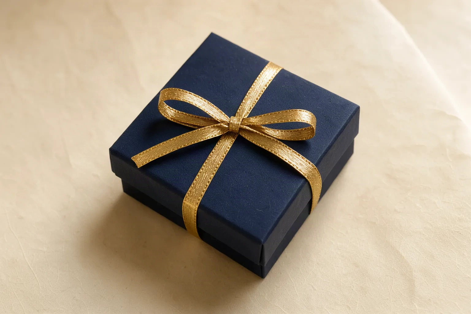 Coffret cadeau bleu nuit fermé par un ruban doré fin, sur fond crème
