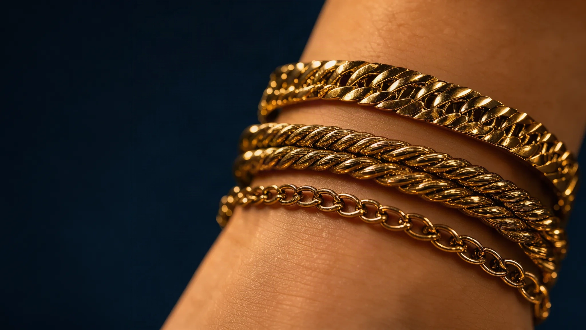 Trois bracelets dorés empilés sur un poignet, fond nuit