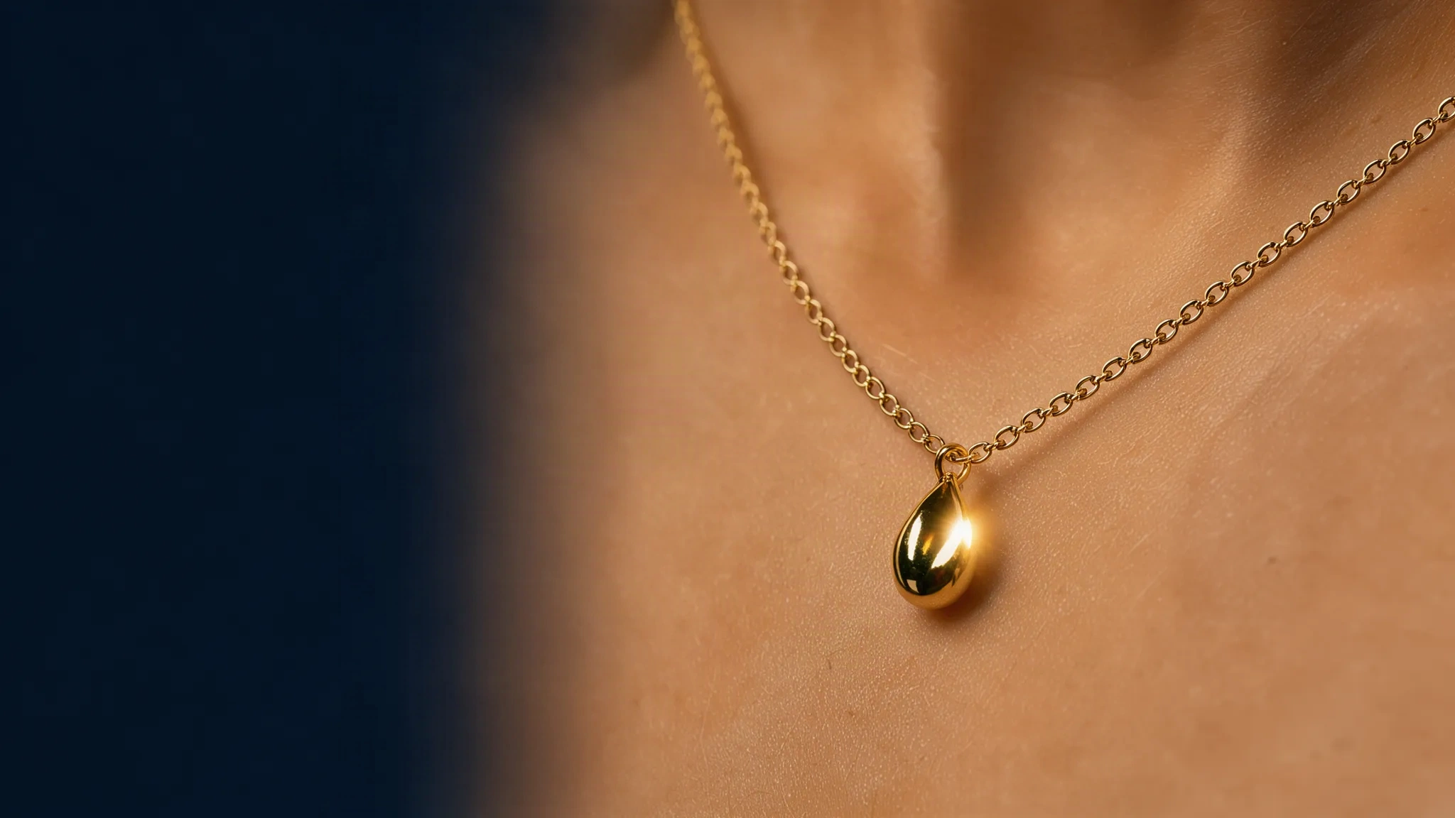 Collier doré à pendentif goutte posé sur une clavicule, fond nuit